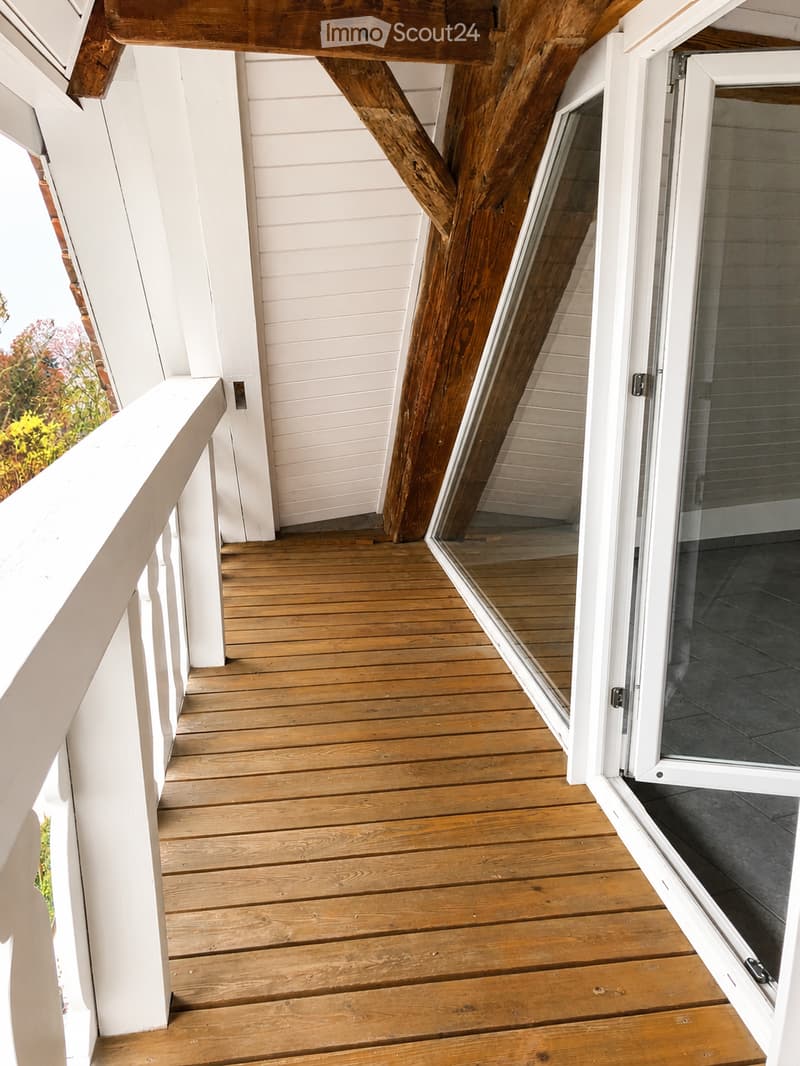 Wooden deck with white railings, open sliding glass door leading inside, visible wooden beams supporting the structure.