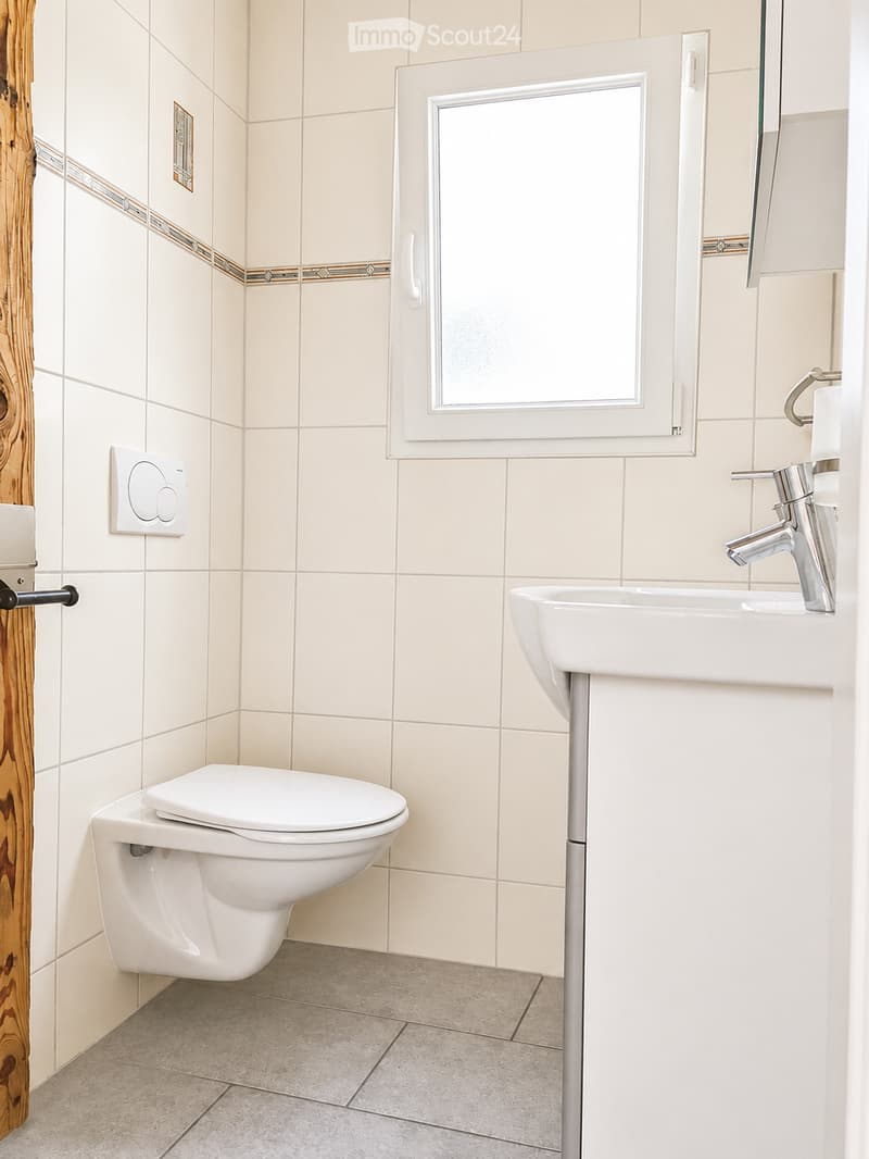 Modern bathroom with white tiles, a toilet, a sink with a chrome faucet, and a window with a frosted glass pane.