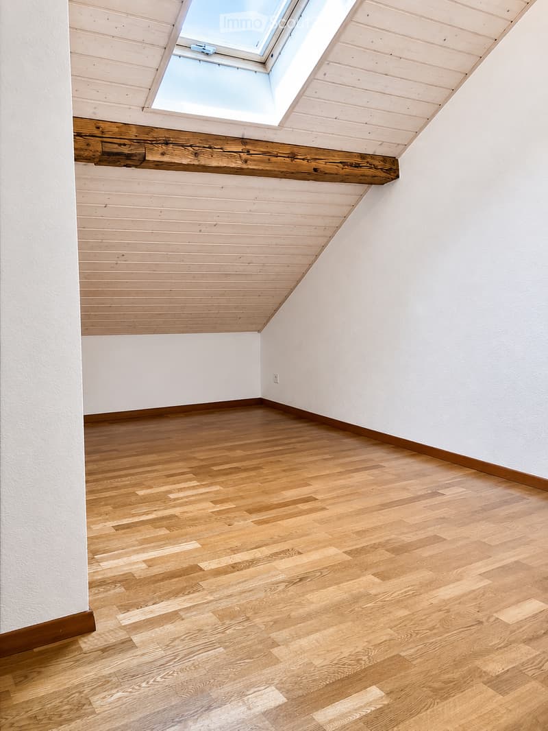 Empty room with wooden flooring, white walls, and a skylight window in the ceiling.