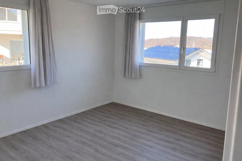 Empty room with light grey walls, wooden flooring, and large windows with curtains. No furniture or equipment present.