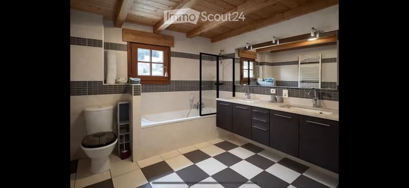 Modern bathroom with a checkered tile floor, dark grey cabinets, a bathtub, toilet, and a large mirror above the sink.