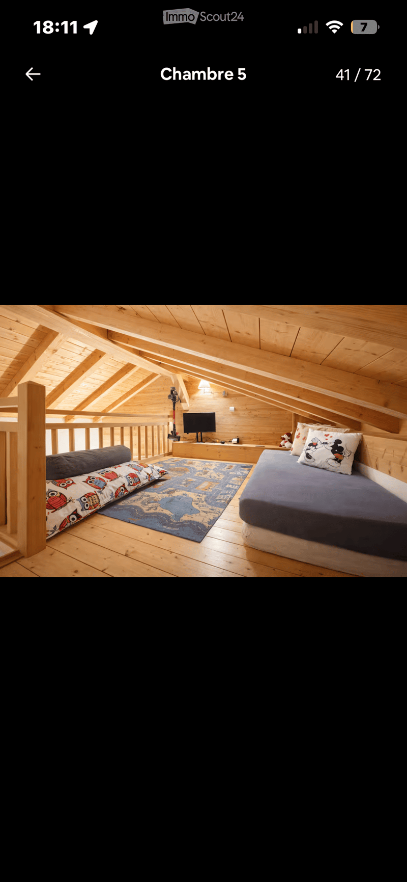 Cozy attic bedroom with wooden beams, a double bed, a sofa, a television, and a colorful rug.