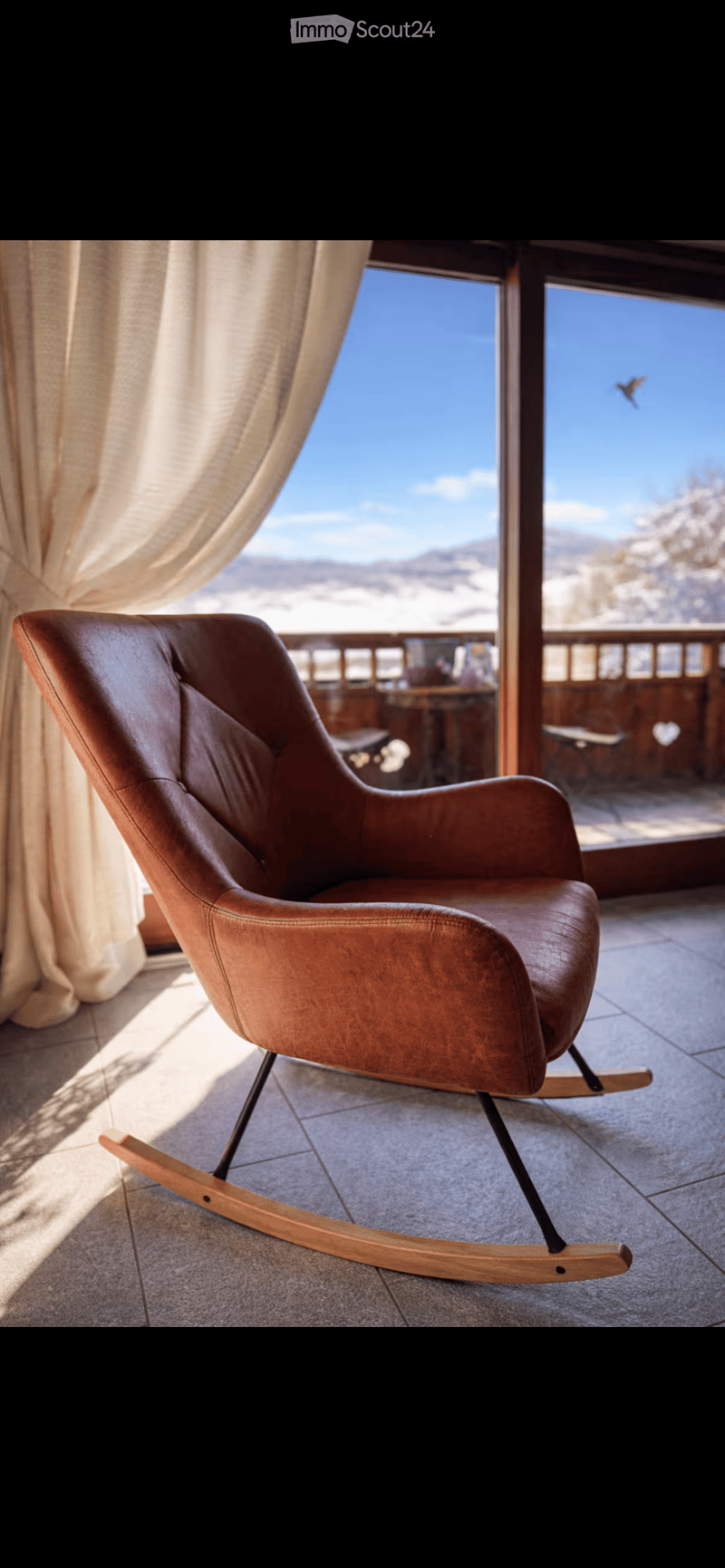 A modern leather rocking chair with wooden base is placed near a large window with a scenic mountain view.