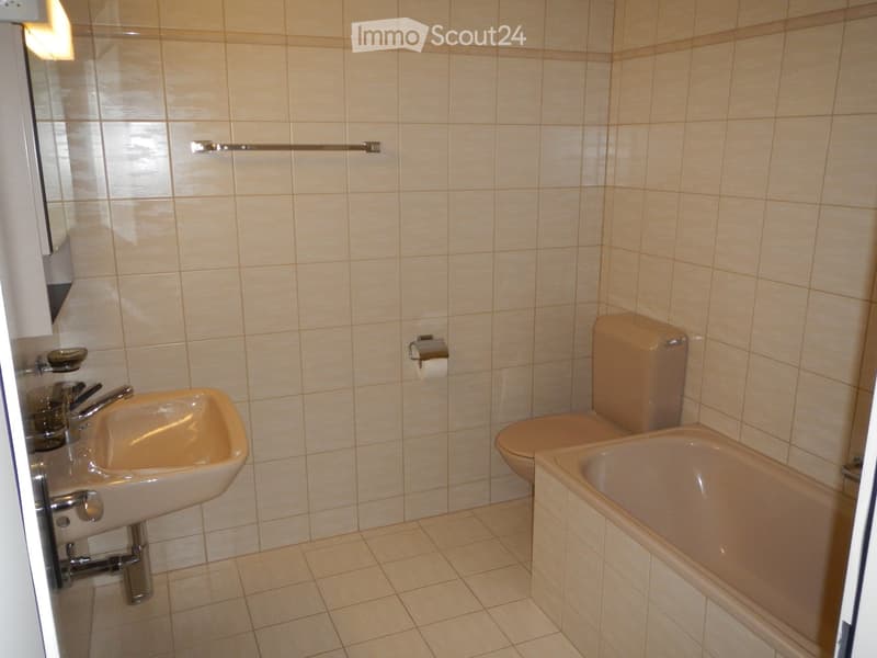 A small bathroom with beige tiles, a sink, a toilet, a bathtub, and a towel rack.
