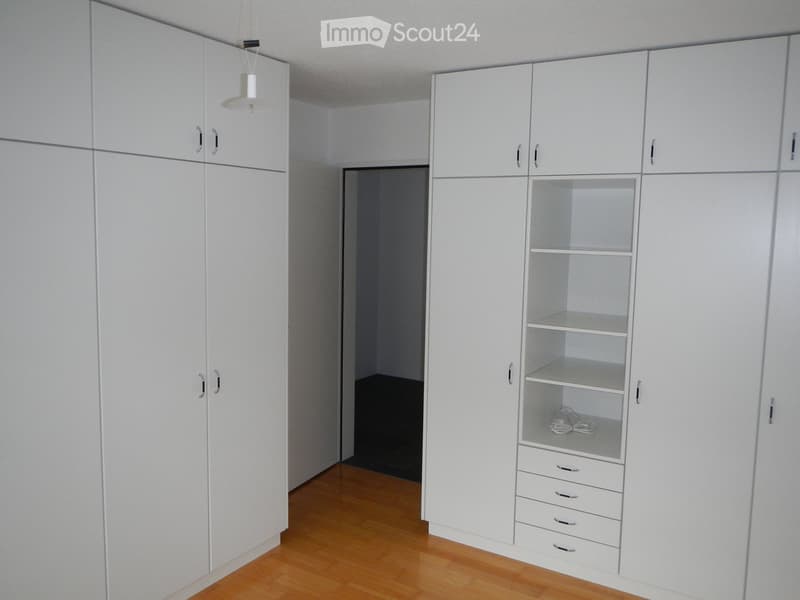 Empty room with white built-in wardrobes, wooden floor, and a small open space in the center.