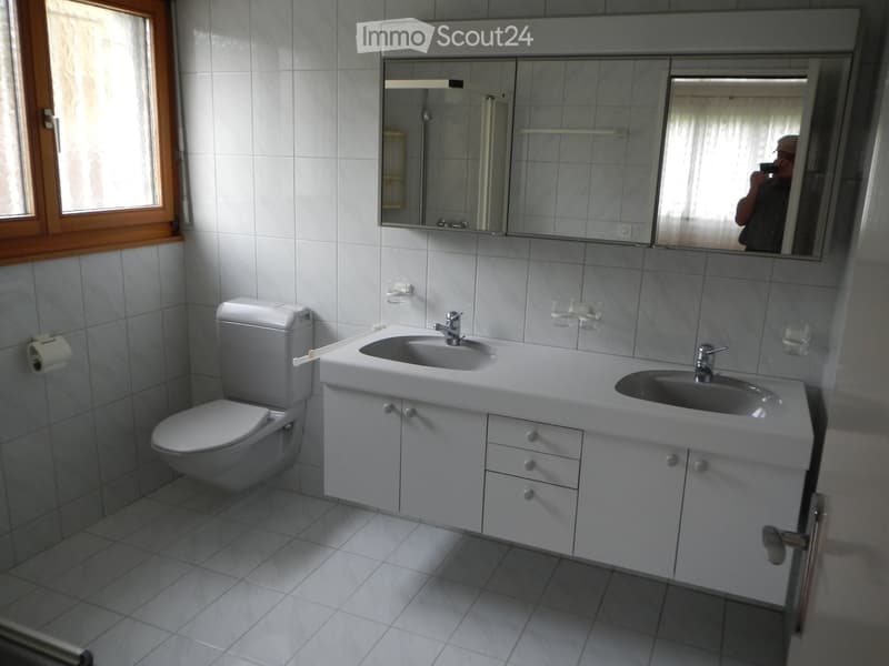 Modern bathroom with white tiles, a double sink vanity, a toilet, and a large mirror above the sink.