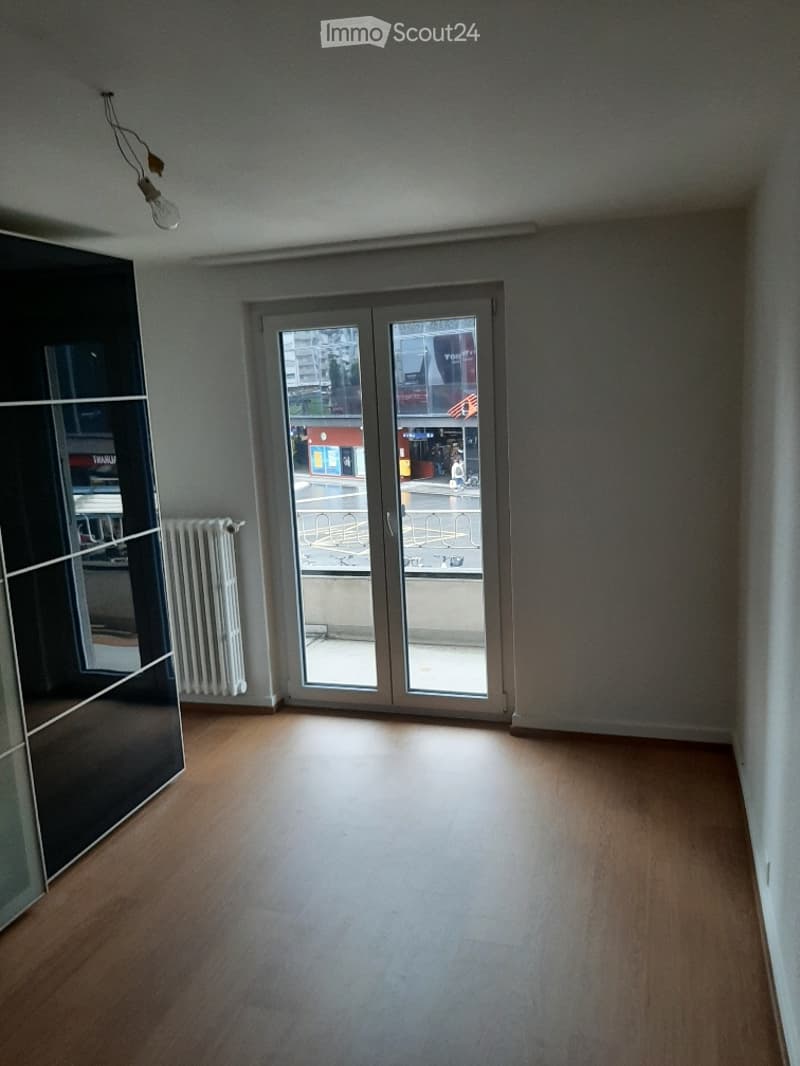 Empty room with wooden flooring, large glass sliding doors leading to a balcony, and a radiator on the wall.