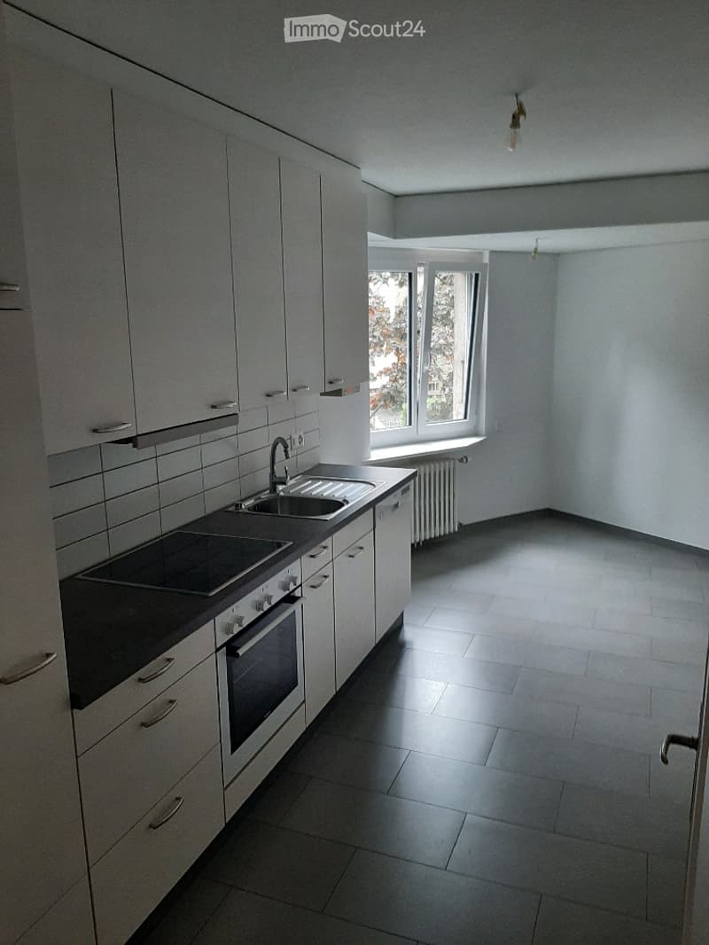 Modern kitchen with white cabinets, black countertop, sink, stove, and oven. The space is well-lit with natural light from a window.