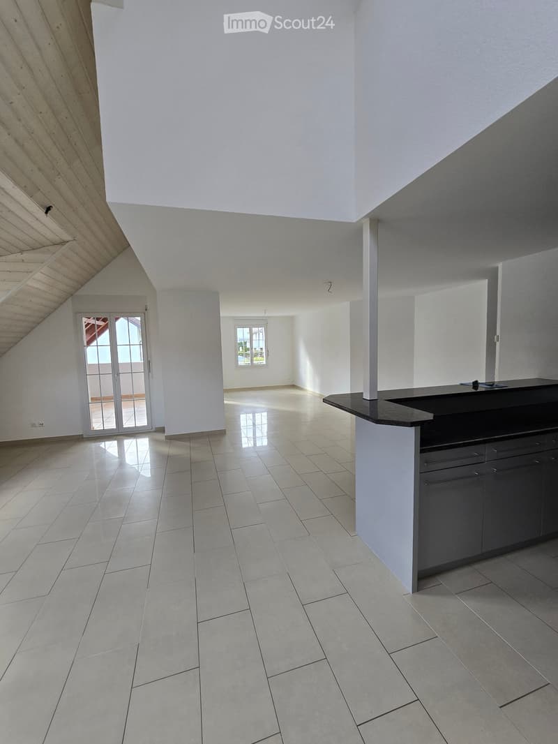 An unfurnished room with white walls, tiled flooring, and a modern kitchen counter. The room features large windows and a sliding glass door leading to an outdoor area.