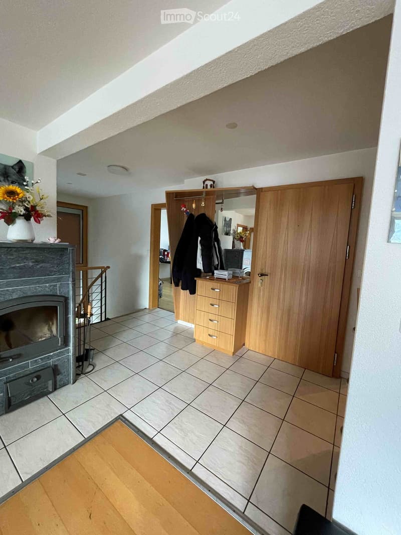 Hallway with tiled floor, wooden door, coat rack, and fireplace with vase of flowers on mantel.