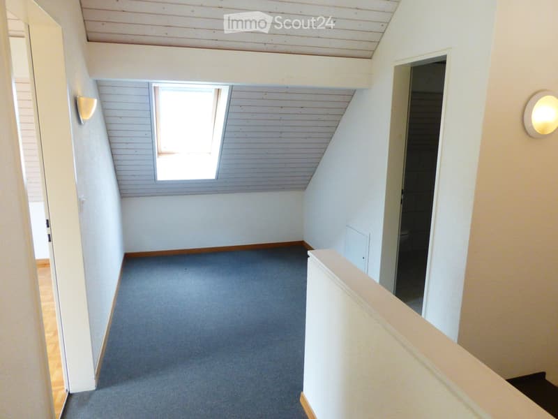 Empty hallway with wooden ceiling, carpeted floor, and white walls. Features a window and a door leading to another room.