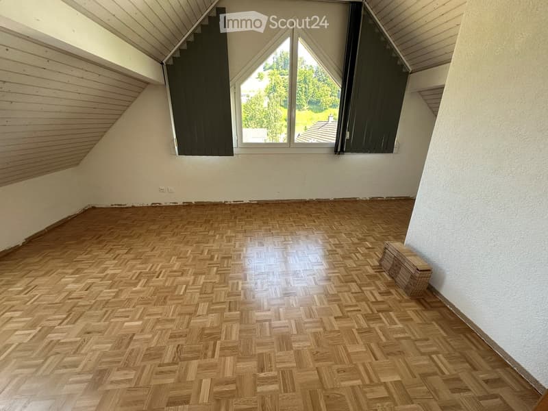 Empty attic room with wooden herringbone flooring, white walls, and large skylight windows.