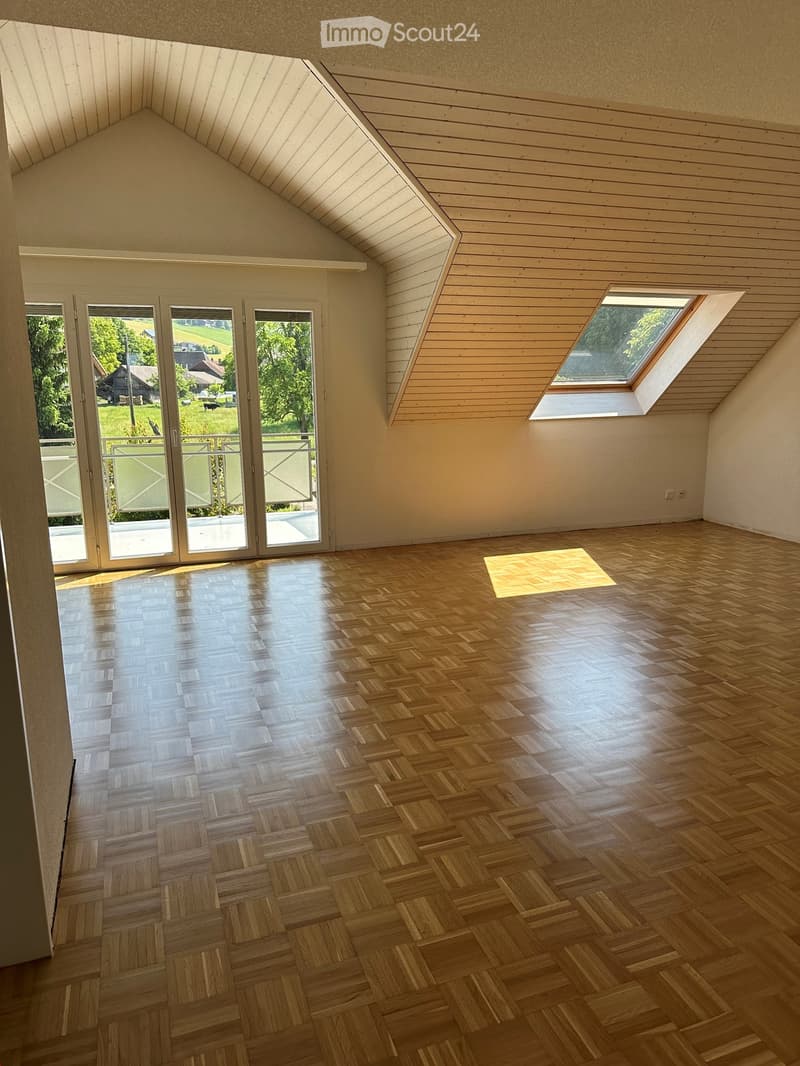 Empty room with wooden herringbone flooring, slanted wooden ceiling, large windows, and a sliding glass door leading to an outdoor area.