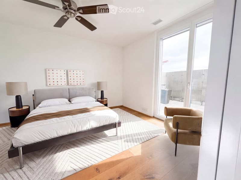 Modern bedroom with a large bed, nightstands, lamps, a chair, and a ceiling fan. Large sliding glass doors lead to a balcony.