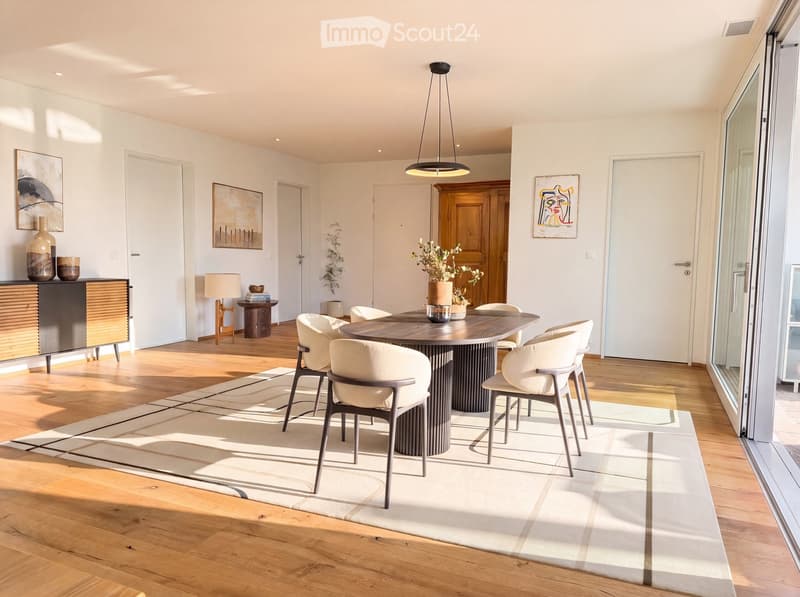 Modern dining room with a round wooden dining table, six chairs, a hanging pendant light, a side table with a lamp, and decorative vases on a cabinet.