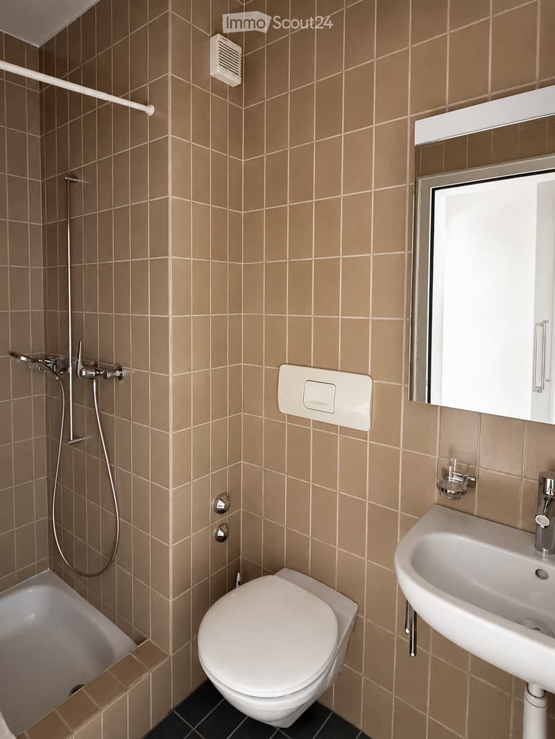 Modern bathroom with beige tiled walls, a white toilet, a sink with a chrome faucet, a bathtub, and a showerhead with a handheld hose.