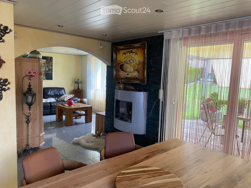 A well-lit living room with a black leather sofa, wooden coffee table, fireplace, dining table with chairs, and decorative items including a lamp and picture frame.
