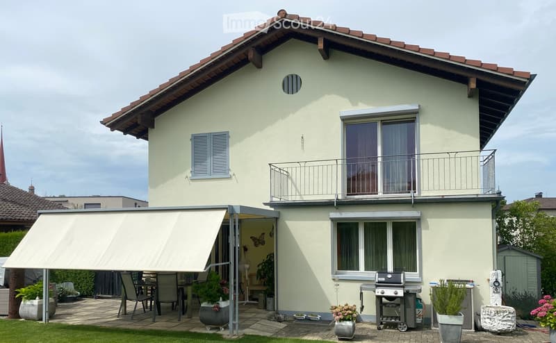 Two-story house with a balcony, patio area with a table, chairs, grill, and potted plants.