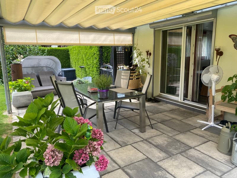 A covered patio with a glass table, chairs, a sofa, a fan, and potted plants.