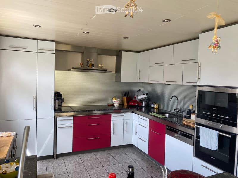 Modern kitchen with white and red cabinets, stainless steel appliances, granite countertops, and various kitchen items on the counters.