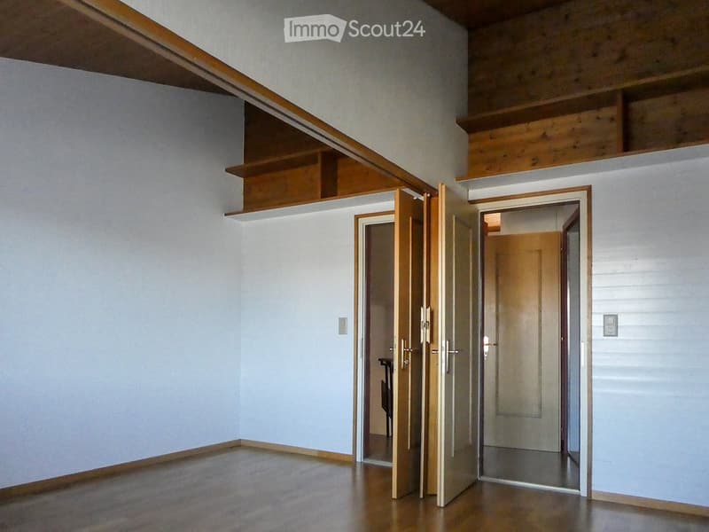 Empty room with wooden flooring, white walls, and built-in wooden shelving. Two open doors lead to adjacent spaces.