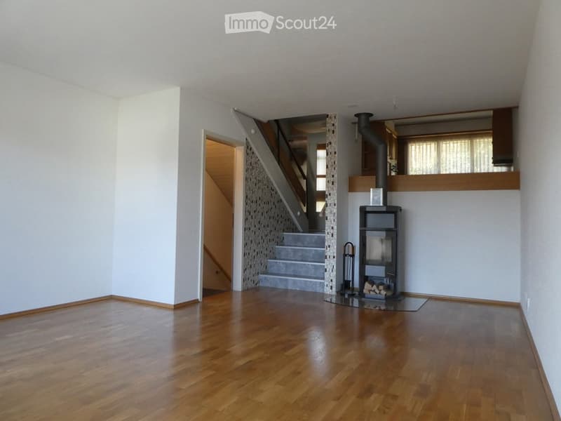 Spacious living room with wooden flooring, a modern fireplace, and a small shelf. A staircase leads to an upper level.