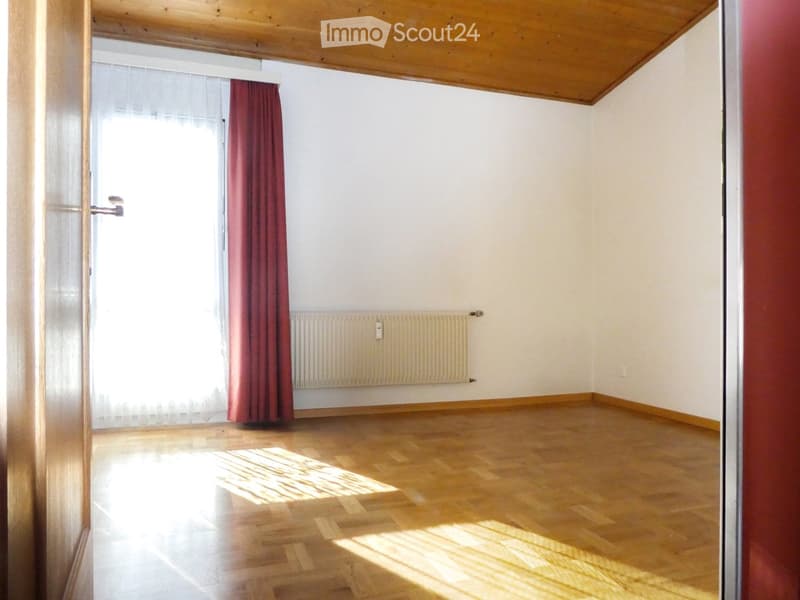 Empty room with wooden flooring, white walls, a radiator, and a window with red curtains.