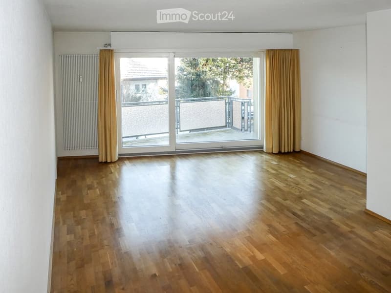Empty room with wooden flooring, large sliding glass doors leading to a balcony, and light-colored walls.