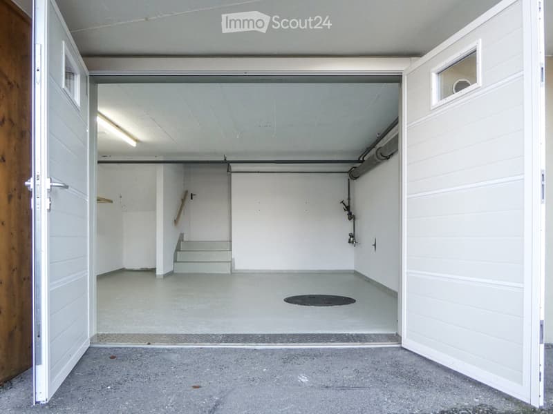 Empty garage with white walls, concrete floor, and a small staircase leading to an upper level. No furniture or equipment present.