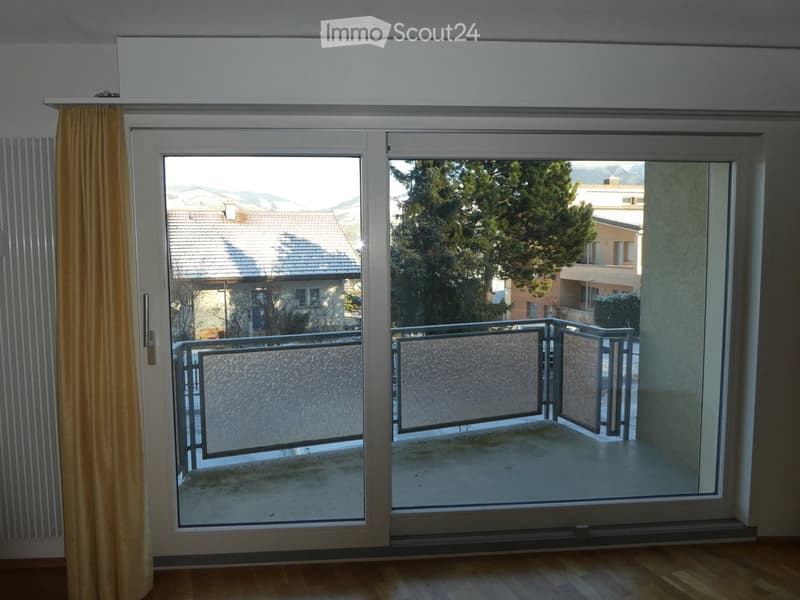 Sliding glass doors open to a balcony with a view of mountains and a neighboring house.