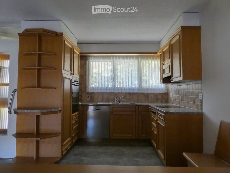Modern kitchen with wooden cabinets, granite countertops, stainless steel appliances, and a large window with blinds.