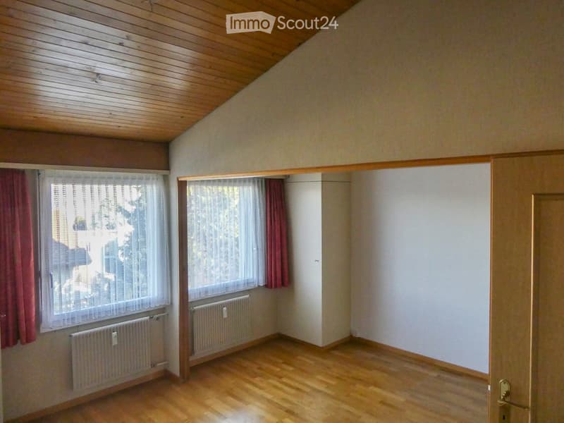 Empty room with wooden flooring, white walls, and large windows with curtains. Radiators are visible beneath the windows.