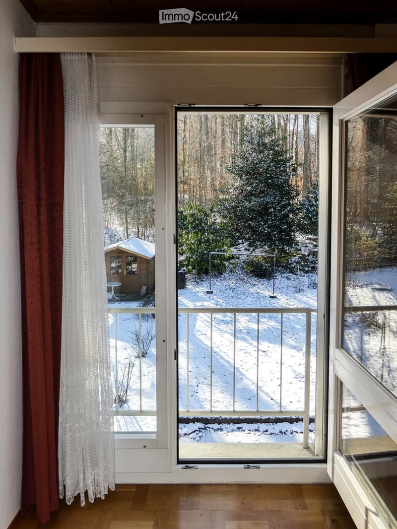 View from a room with large windows showing a snowy outdoor area, trees, and a small wooden structure.