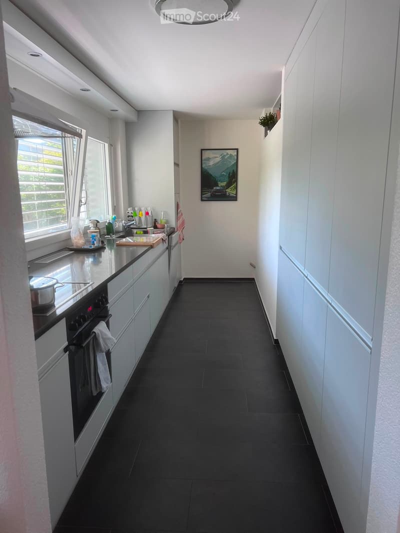 Modern kitchen with white cabinets, black tiled floor, and stainless steel appliances. Features an oven, sink, and various kitchen items on the counter.