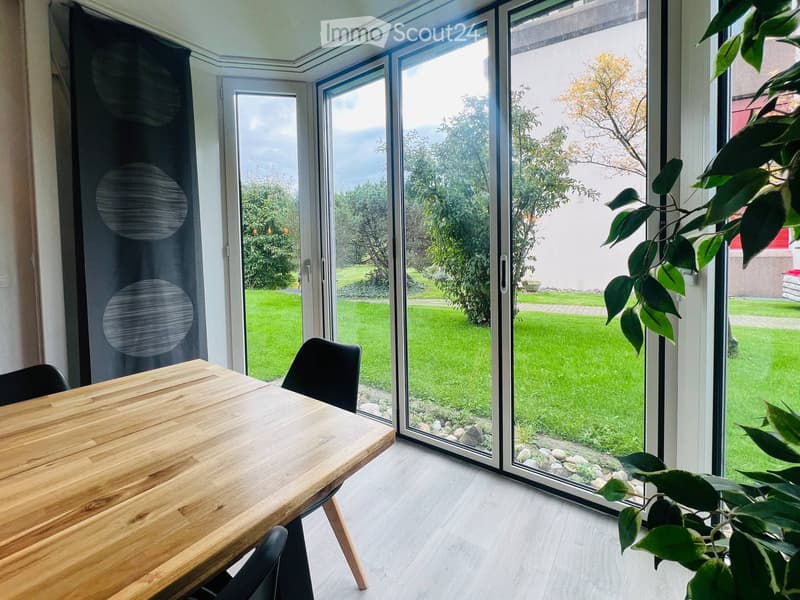 Bright dining area with large sliding glass doors opening to a green garden, wooden table, and black chairs.