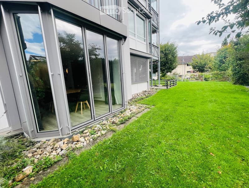 Modern house exterior with large glass sliding doors leading to a patio, surrounded by a well-maintained lawn and small rock border.