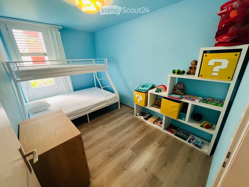 Brightly colored children's bedroom with a bunk bed, a white shelving unit filled with toys and books, and a wooden cabinet.
