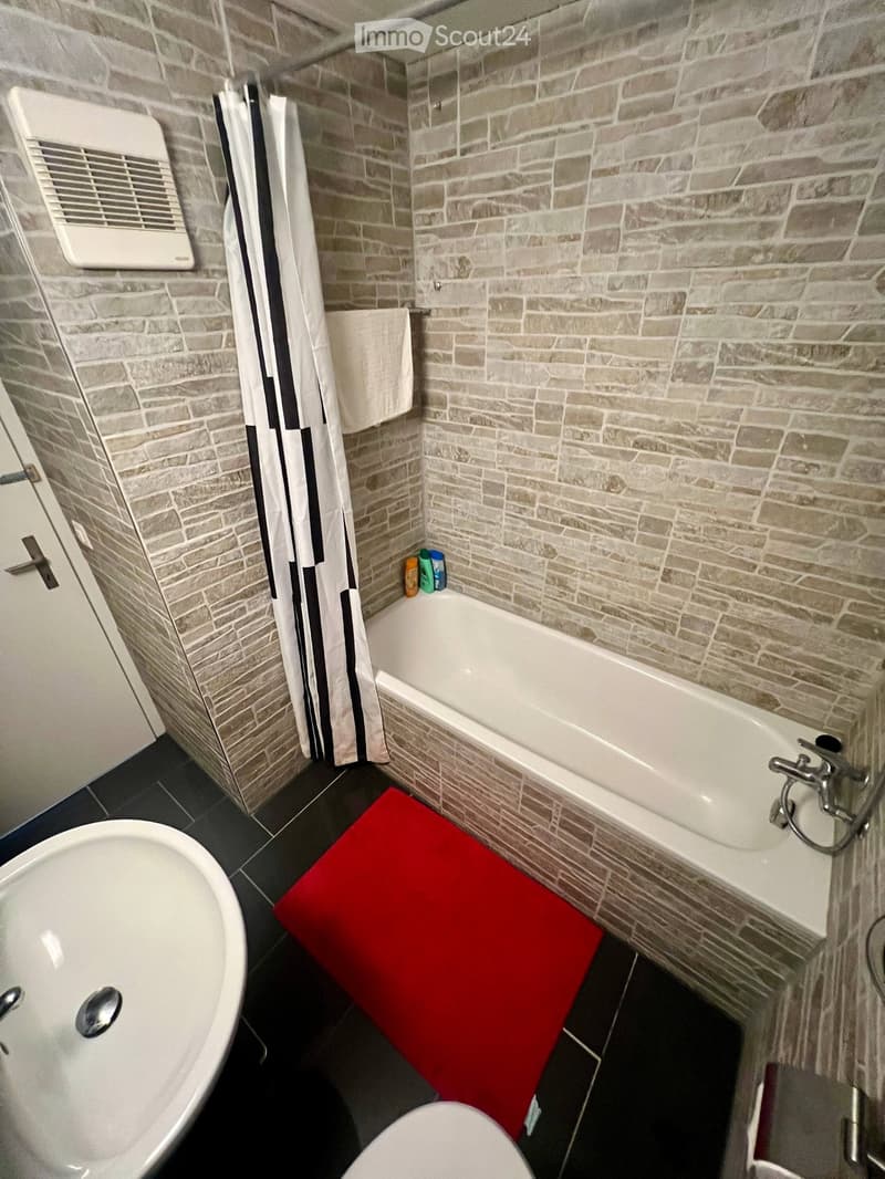 Bathroom with a bathtub, toilet, shower curtain, and a red bath mat on the floor.