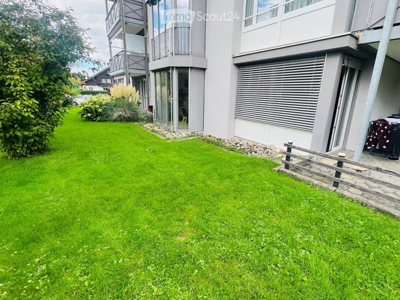 Well-maintained lawn with a modern building in the background, featuring balconies and large windows.