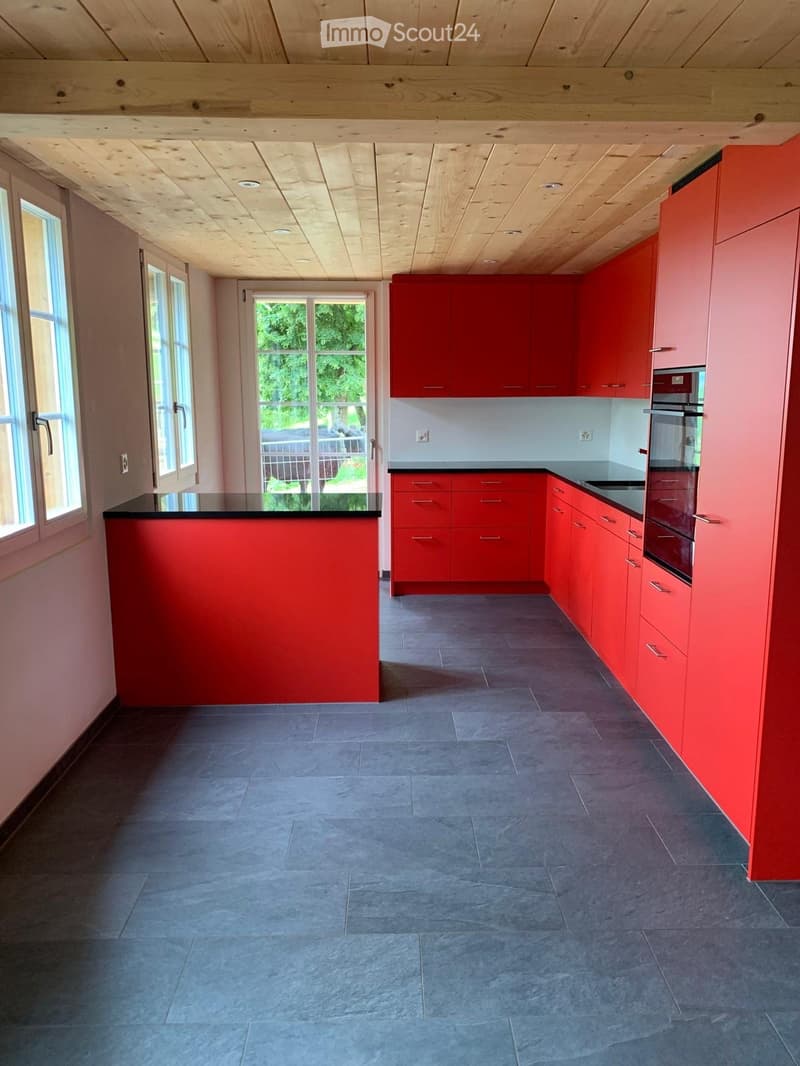 Modern kitchen with red cabinets, grey tiled floor, and large windows offering a view of the garden.