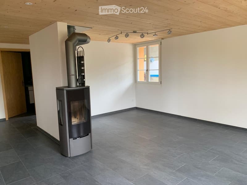 Empty room with a modern wood-burning stove, grey tiled floor, white walls, and a large window.