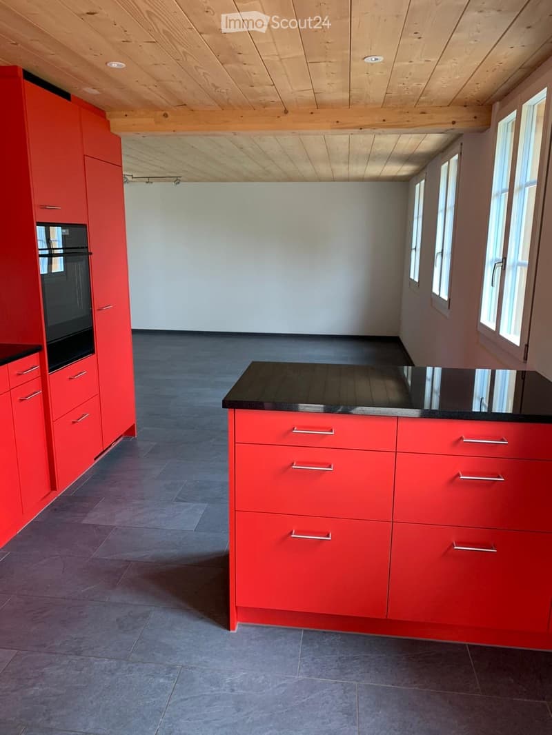 Modern kitchen with red cabinets, black countertop, and grey tiled floor. Features large windows and a sleek design.