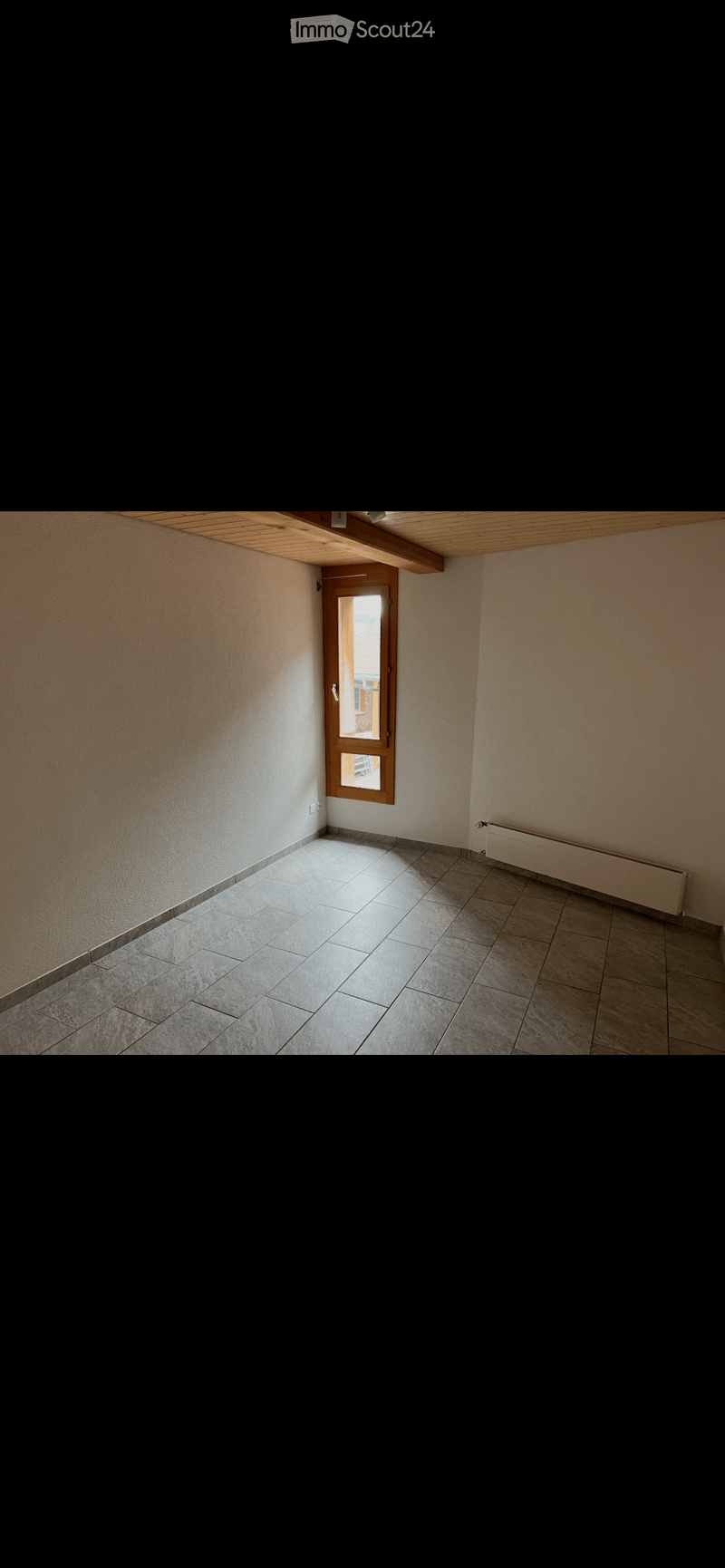 Empty room with tiled floor, white walls, wooden door with glass panel, and radiator on one wall.