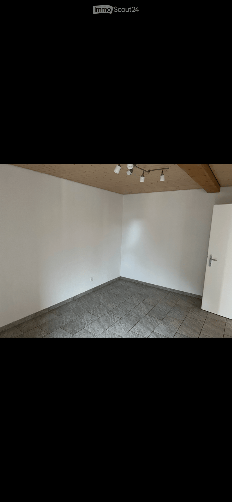 Empty room with white walls, grey tiled floor, and a wooden ceiling with track lighting. No furniture or equipment present.