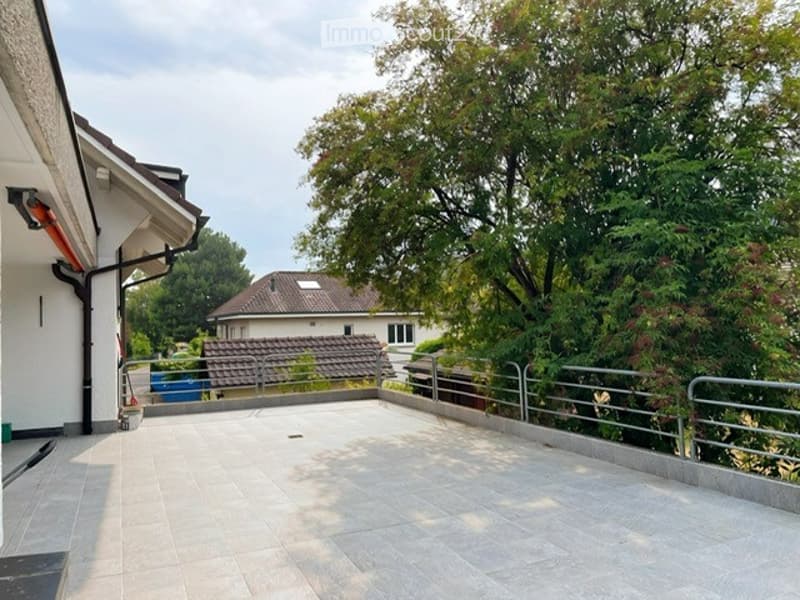 Roof terrace with tiled flooring, metal railing, and views of surrounding houses and greenery.