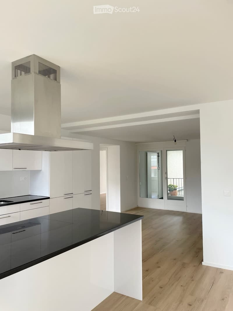 Modern kitchen with white cabinets, black countertops, and a central island. Features a large range hood and a sliding glass door leading to a balcony.