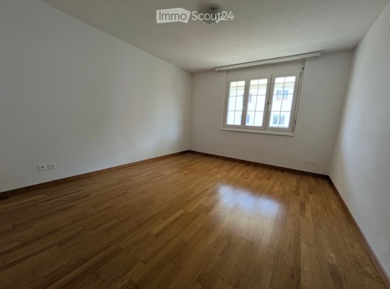 Empty room with wooden flooring, white walls, and a single window with white frame and multiple panes.