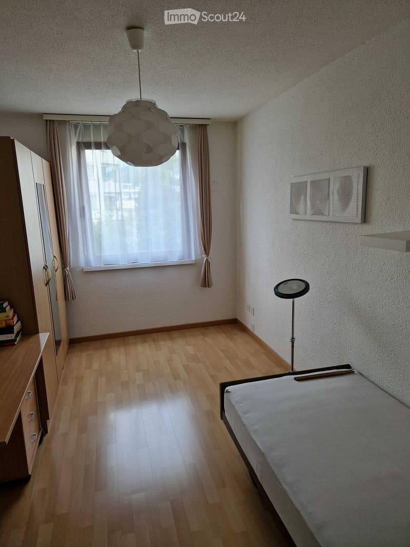 Minimalist bedroom with wooden flooring, a single bed, a wardrobe, a hanging lamp, and a mirror on the wall.