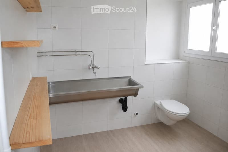 Modern bathroom with white tiled walls, a wooden shelf, a stainless steel sink, and a white toilet.