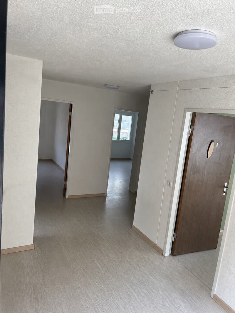 Empty hallway with light-colored walls, wooden flooring, and several doors leading to other rooms.